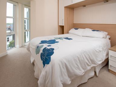 A bedroom with a double bed with floral bedding near a window at The Moorings in Deganwy near Llandudno