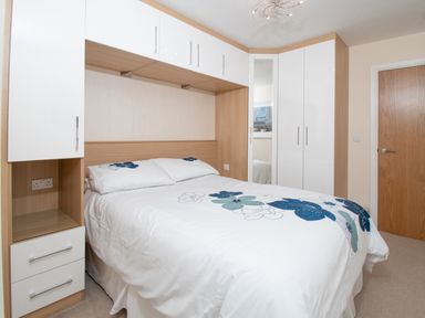 A bedroom with a double bed and built in white and wood storage units at The Moorings in Deganwy near Llandudno