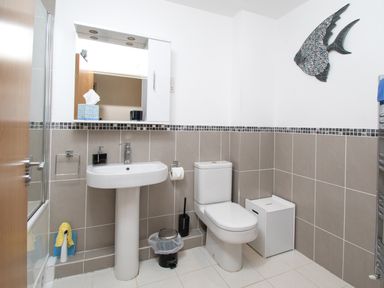 A bathroom with a sink toilet trash can and wall decoration at The Moorings in Deganwy near Llandudno