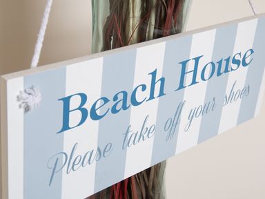 A sign with blue and white stripes that reads Beach House Please take off your shoes