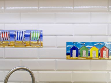 A white tiled wall with decorative tiles of beach chairs and colorful beach huts at The Moorings in Deganwy near Llandudno