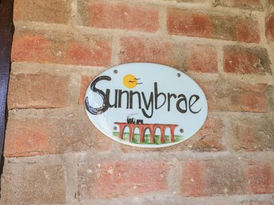 An oval ceramic sign with the word Sunnybrae and a drawing of a train on a bridge attached to a brick wall at Sunnybrae in Whitby