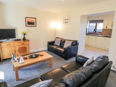 A living room with black leather sofas a wooden coffee table a wooden TV stand a television and an open doorway to a kitchen at Sunnybrae in Whitby