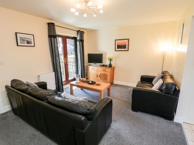 A living room with two black leather sofas a wooden coffee table a wooden cabinet a television and curtains at Sunnybrae Whitby