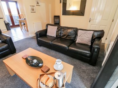 A living room with black leather sofas a wooden coffee table with pastries and a coffee pot at Sunnybrae Whitby