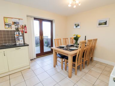 A dining area with a wooden table and eight chairs near glass patio doors at Sunnybrae in Whitby
