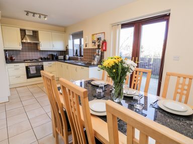 A kitchen and dining area with wooden chairs around a table set with plates and a vase of flowers at Sunnybrae in Whitby