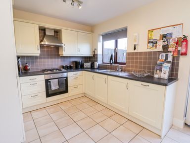 A kitchen with cream cabinets black countertops a gas stove oven a sink under a window and a corkboard with notices at Sunnybrae in Whitby
