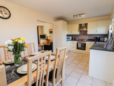 A kitchen and dining area with a dining table set with plates and a vase of flowers and an adjoining living room with a television at Sunnybrae Whitby