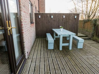 An outdoor deck area with a wooden picnic table and benches and flower pots on the fence and table at Sunnybrae in Whitby
