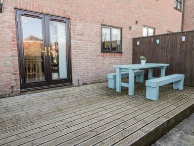 A wooden deck with a blue picnic table and benches next to a brick wall and dark brown door at Sunnybrae in Whitby