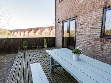 An outdoor wooden deck with a light blue picnic table and potted plant with a brick house wall and glass doors in the background at Sunnybrae Whitby