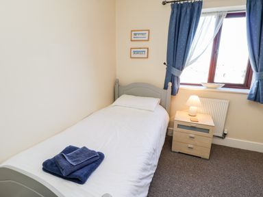 A single bed with folded towels on it beside a nightstand with a lamp and window with blue curtains at Sunnybrae in Whitby