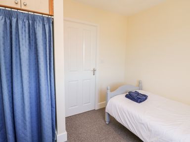A bedroom with a single bed with towels on it a door and a blue curtain at Sunnybrae in Whitby