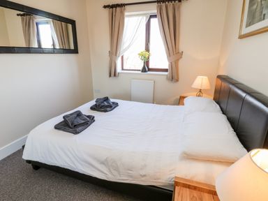 A bedroom with a bed with white linens two folded towels bedside tables lamps a window with curtains and a mirror on the wall at Sunnybrae in Whitby