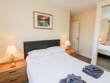 A bedroom with a double bed white bedding two bedside tables with lamps framed picture above the bed and folded towels on the bed at Sunnybrae in Whitby