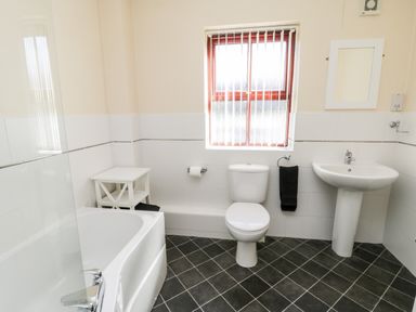 A bathroom with a bathtub a toilet a pedestal sink small white table and a window at Sunnybrae in Whitby