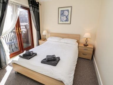 A bedroom with a double bed two bedside tables lamps curtains and glass doors leading to an outdoor seating area at Sunnybrae in Whitby