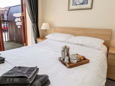 A bedroom with a made bed white linens two pillows a bedside lamp wooden nightstands and a tray with cups and a French press at Sunnybrae in Whitby