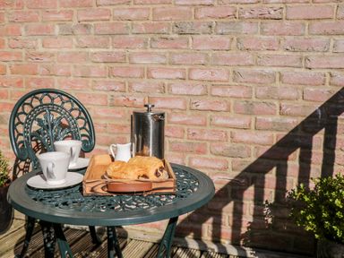 A metal outdoor table with two cups saucers a tray with croissants a milk jug and a metal French press against a brick wall at Sunnybrae in Whitby