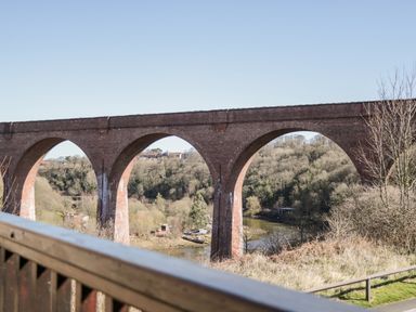 A view of a brick railway viaduct with arches over a river and trees at Sunnybrae in Whitby