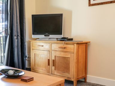 A wooden cabinet with a television and electronic devices on top beside a window with curtains at Sunnybrae in Whitby