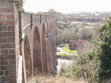 A brick arch bridge over a river with houses and trees in the background at Sunnybrae in Whitby