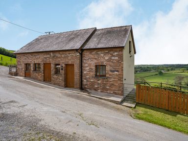 A brick house with wooden doors and windows near a gravel road and green fields at Bwthyn-y-Rhiw Penybanc near Llandeilo