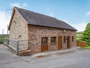 A brick and stone house with wooden windows and doors by a paved road at Bwthyn-y-Rhiw Penybanc near Llandeilo
