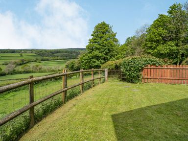 A backyard with grass and wooden fences overlooking green fields at Bwthyn-y-Rhiw in Penybanc near Llandeilo