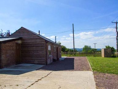 A single-story brick and wood building next to a driveway and grassy area with utility poles in a rural setting at Dovetail Westbury-on-Severn