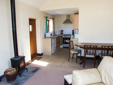 A kitchen and dining area with a wood stove and a beige sofa at Dovetail in Westbury-on-Severn