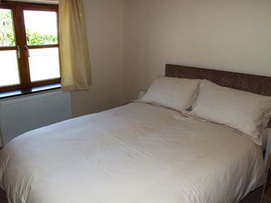 A bedroom with a double bed and pillows next to a window with curtains at Dovetail in Westbury-on-Severn