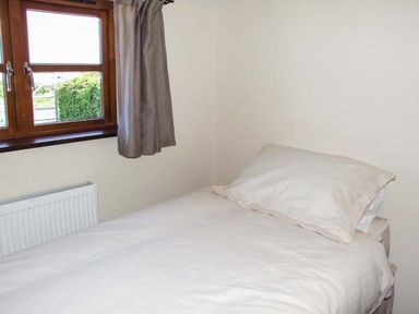 A bedroom with a single bed covered with white bedding next to a window with curtains at Dovetail in Westbury-on-Severn
