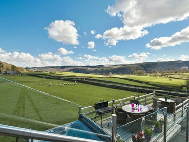 An outdoor deck with tables chairs and a barbecue overlooking a green field with sheep and hills at Browside in Little Arrow near Coniston