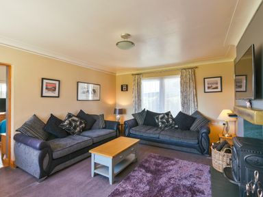A living room with two sofas a coffee table a purple rug a wood stove and framed pictures on walls at Browside Little Arrow near Coniston