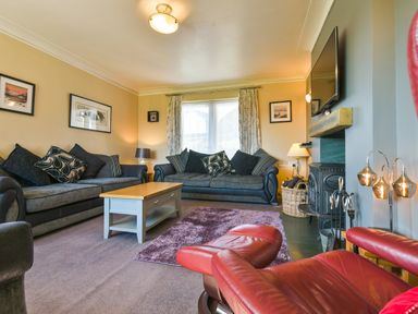 A living room with two grey sofas a wooden coffee table a red leather chair a fireplace and wall-mounted tv at Browside Little Arrow near Coniston