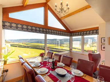 A dining room with a wooden table set with plates and glasses and large windows showing countryside views at Browside in Little Arrow near Coniston