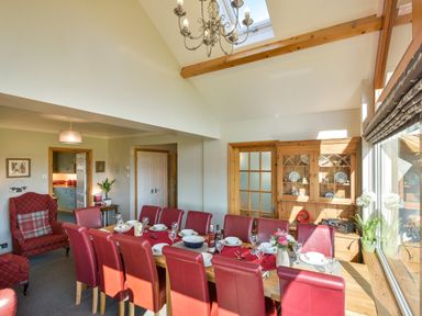 A dining room with a long wooden table set with dishes and red chairs at Browside in Little Arrow near Coniston