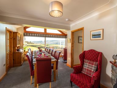 A dining room with a long table set for dinner red chairs a red armchair and large windows showing a landscape at Browside Little Arrow near Coniston
