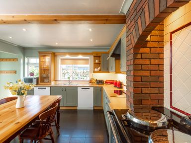 A kitchen with wooden dining table and chairs a brick oven arch and a countertop with red appliances at Browside Little Arrow near Coniston