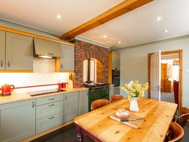 A kitchen with green cabinets wooden table with flowers and bread near a brick arch at Browside Little Arrow near Coniston