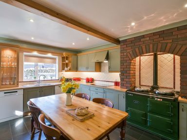 A kitchen with wooden dining table and chairs a green oven and cabinets and a window above the sink at Browside Little Arrow near Coniston