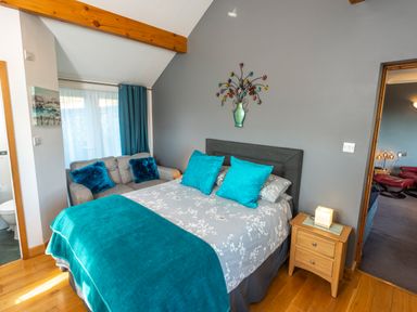 A bedroom with a bed blue pillows blue throw a gray sofa with blue cushions wooden nightstand and wall decoration at Browside Little Arrow near Coniston
