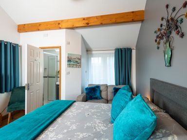 A bedroom with a bed with blue cushions and a gray sofa near a window with blue curtains at Browside Little Arrow near Coniston