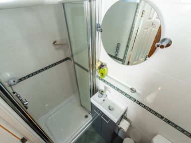 A small bathroom with a shower area a round mirror a sink with cabinet and toiletries at Browside Little Arrow near Coniston