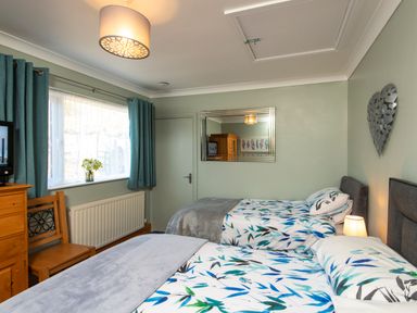A bedroom with two single beds with patterned bedding a wooden chair and chest of drawers a window with curtains a wall mirror and a heart-shaped wall decoration at Browside Little Arrow near Coniston