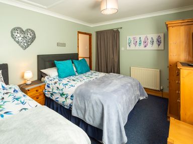 A bedroom with two beds a wooden dresser a nightstand with lamp and artwork on walls at Browside Little Arrow near Coniston