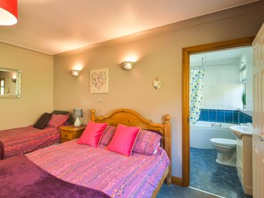 A bedroom with two beds and an open door showing a bathroom with a bathtub at Browside in Little Arrow near Coniston