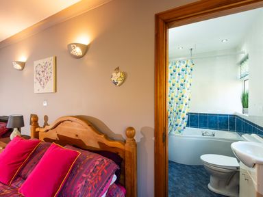 A bedroom with a wooden bed and pink pillows next to a bathroom with a bathtub and pineapple shower curtain at Browside Little Arrow near Coniston